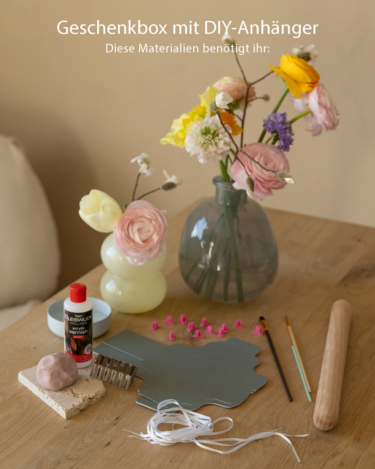 Material für kleine Geschenkanhänger ausgebreitet auf einem Tisch, im Hintergrund zwei Vasen mit Frühlingsblumen