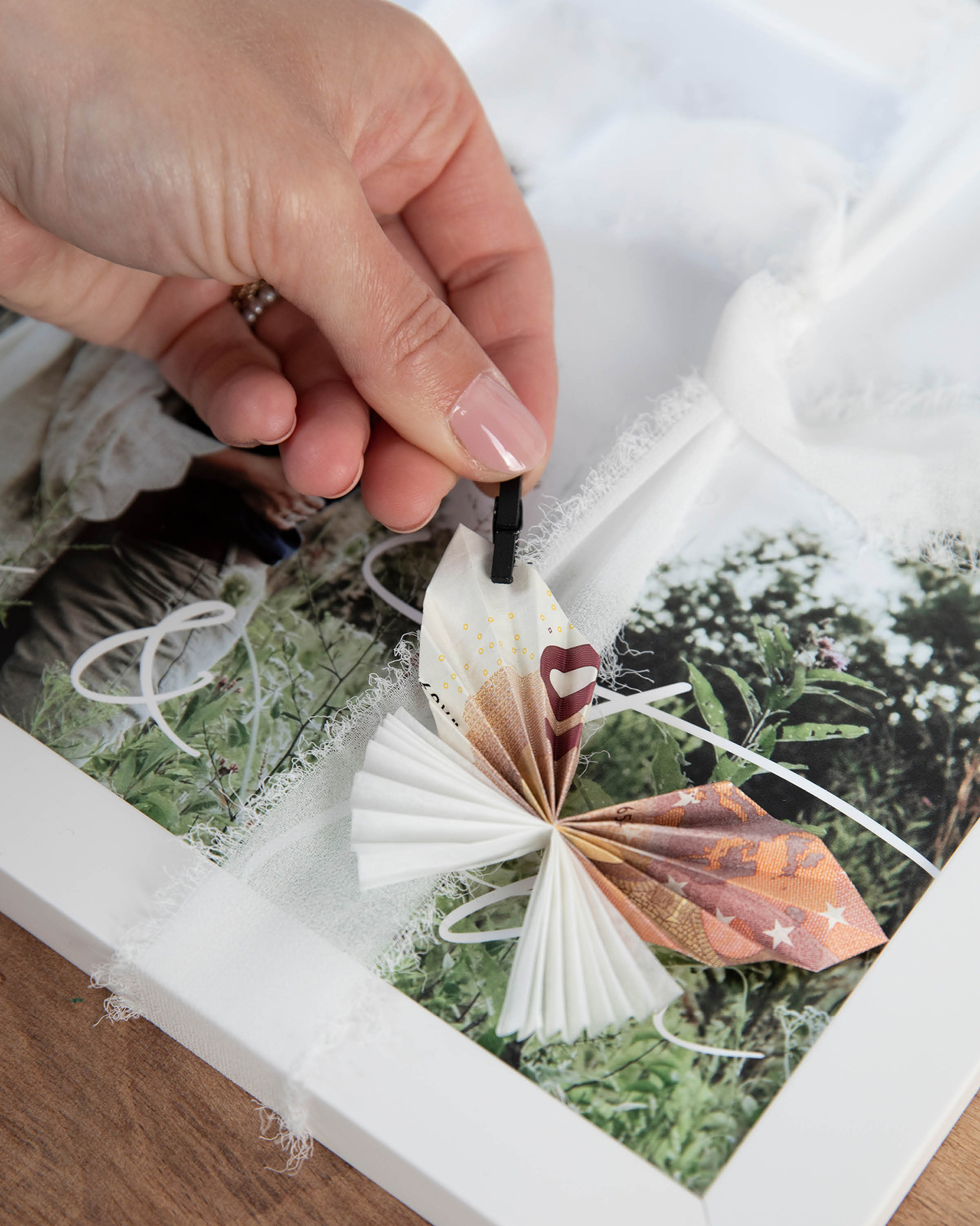 Schmetterling aus Geldscheinen wird mit Wäscheklammer an Wandbild befestigt. 