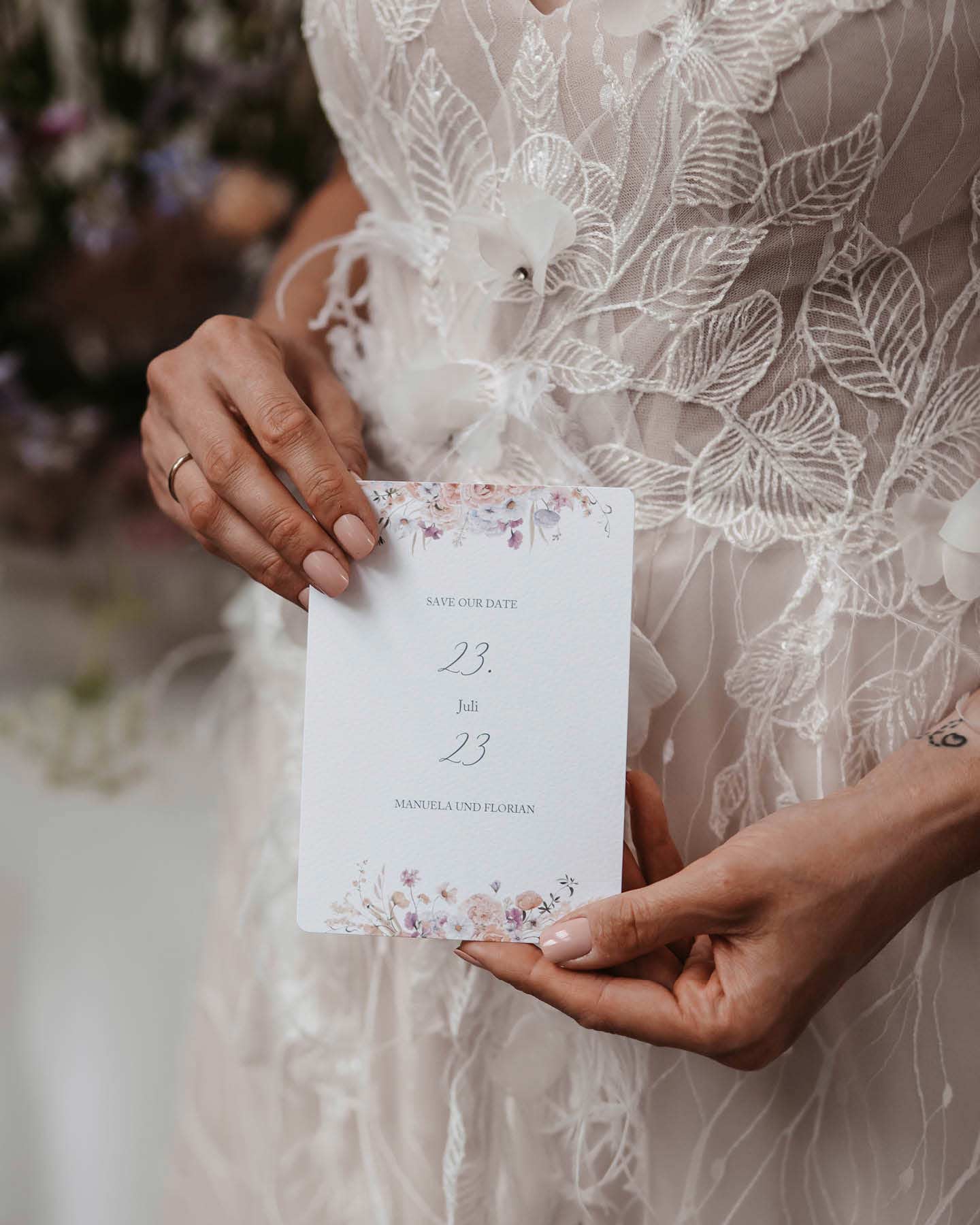 Floral Chic Save-the-Date-Karte: gezeichnete Wildblumen säumen den Rand einer Karte, die die Braut in den Händen hält.