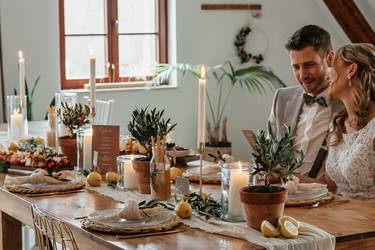 Braut und Bräutigam sitzen gemeinsam an der geschmückten Hochzeitstafel.