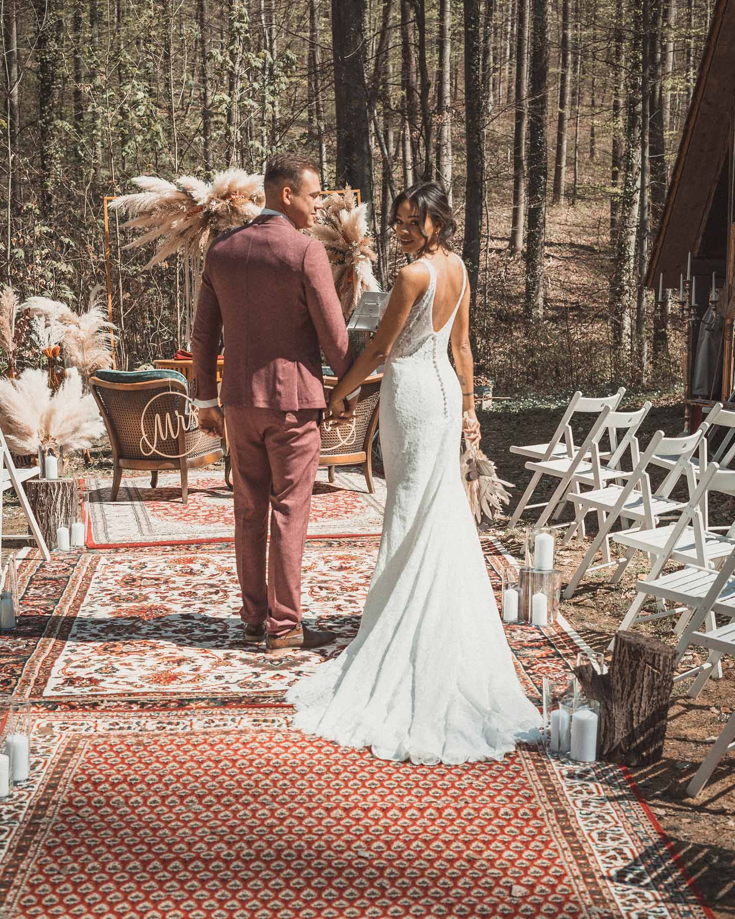 Vintage boho Brautpaar läuft auf Teppichen im Wald zum Traualter.