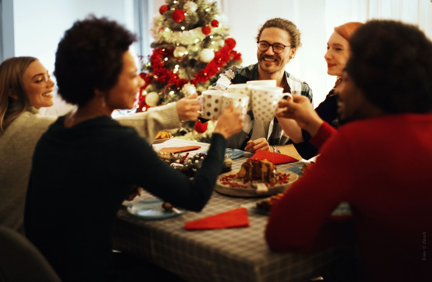 Freunde stoßen an einem weihnachtlich gedeckten Tisch miteinander an.