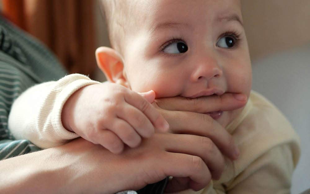 Baby beißt in Finger der Mutter