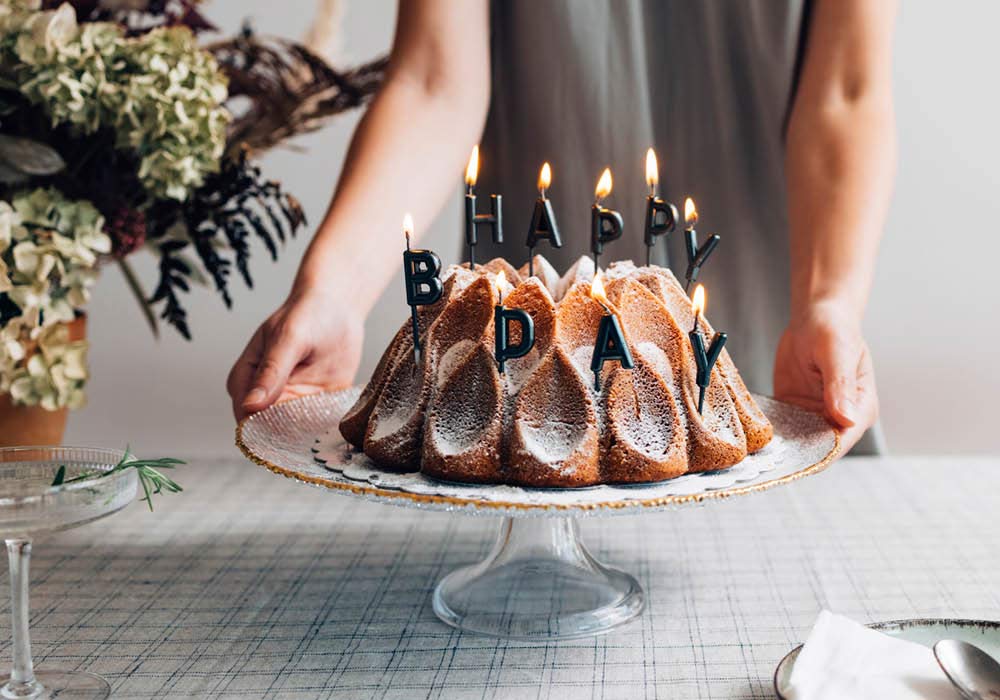 Geburtstagskuchen mit schwarzen Happy B-Day Kerzen wird auf einen Tisch gestellt.
