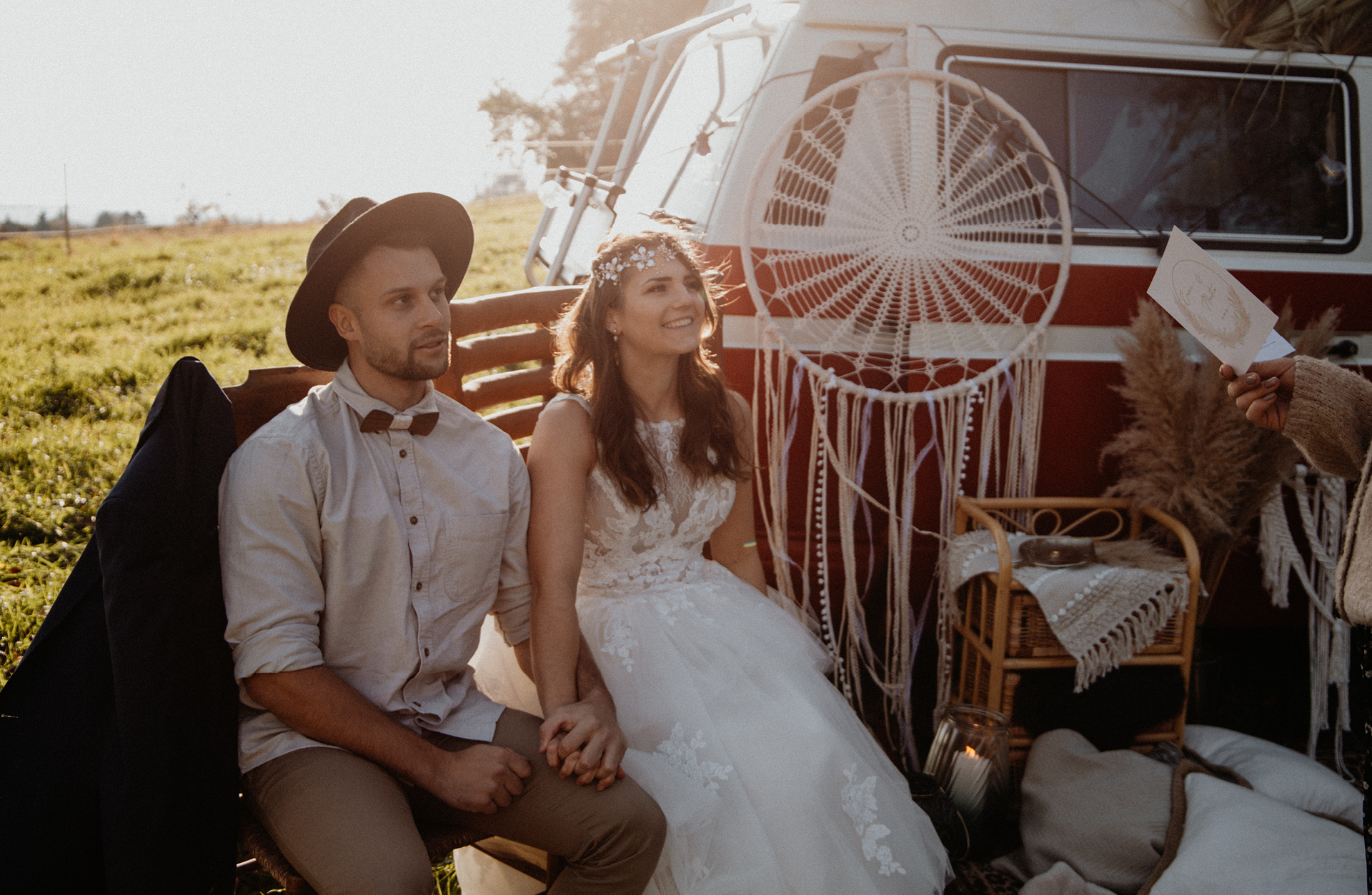 Verliebtes Brautpaar sitzt auf Holzstühlen und wird im Freien von einer Traurednerin getraut bei ihrer Picknick Hochzeit.