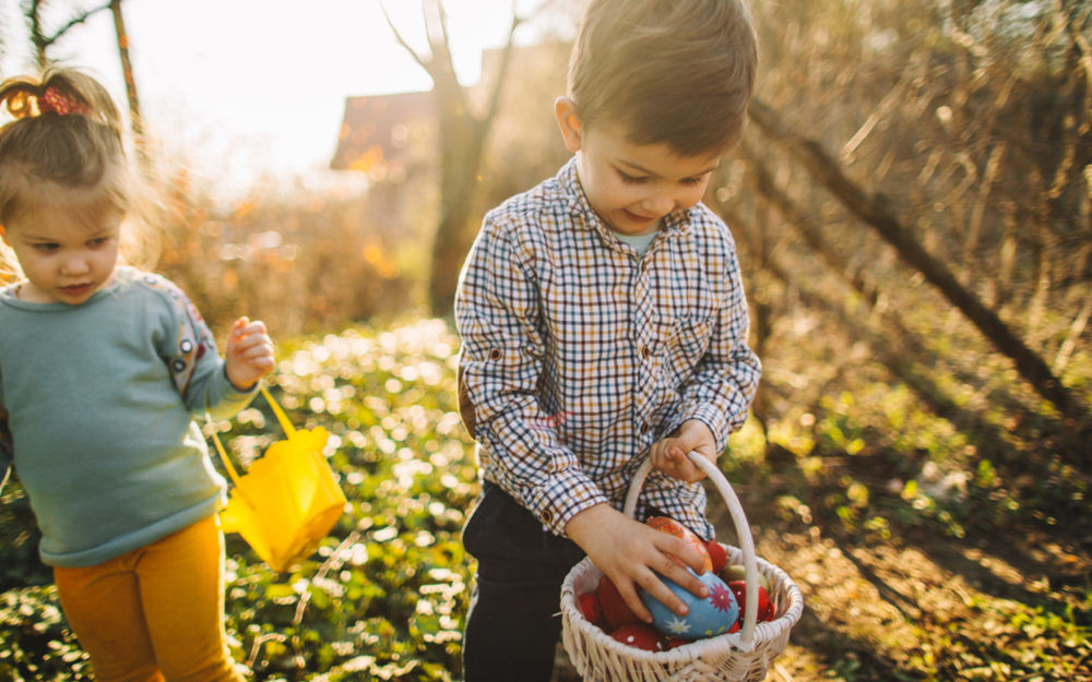Osterwünsche: Kinder suchen Ostereier im Garten