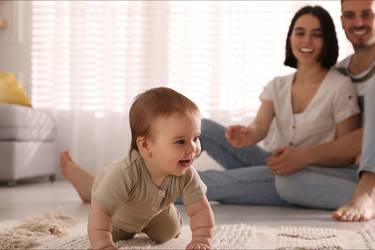 Baby krabbelt auf dem Boden, im Hintergund lachende Eltern