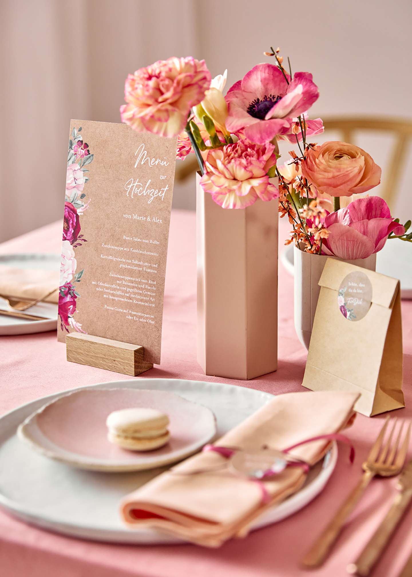 Tischpapeterie liebevoll dekoriert in soften und leuchtenden Pinktönen. Die Blumen auf dem Tisch passen farblich zur Tischdeko und ein Maccaron schmückt den gedeckten Teller.