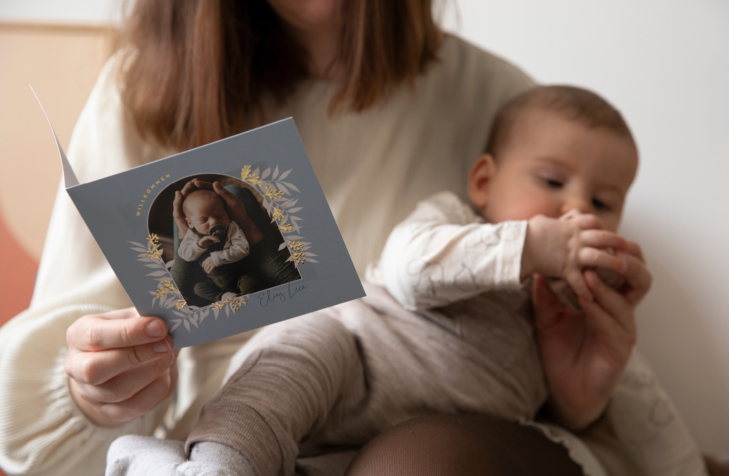 Mutter mit Baby im Arm schaut sich Geburtskarte an