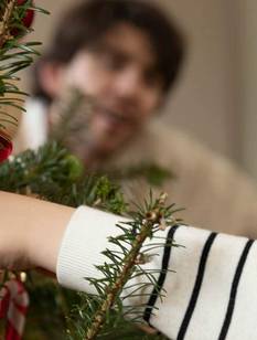 Kleiner Junge hängt Weihnachtsbaumschmuck auf.