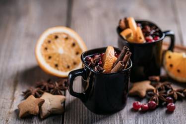 Zwei Tassen mit Feuerzangenbowle stehen auf einem Holztisch.