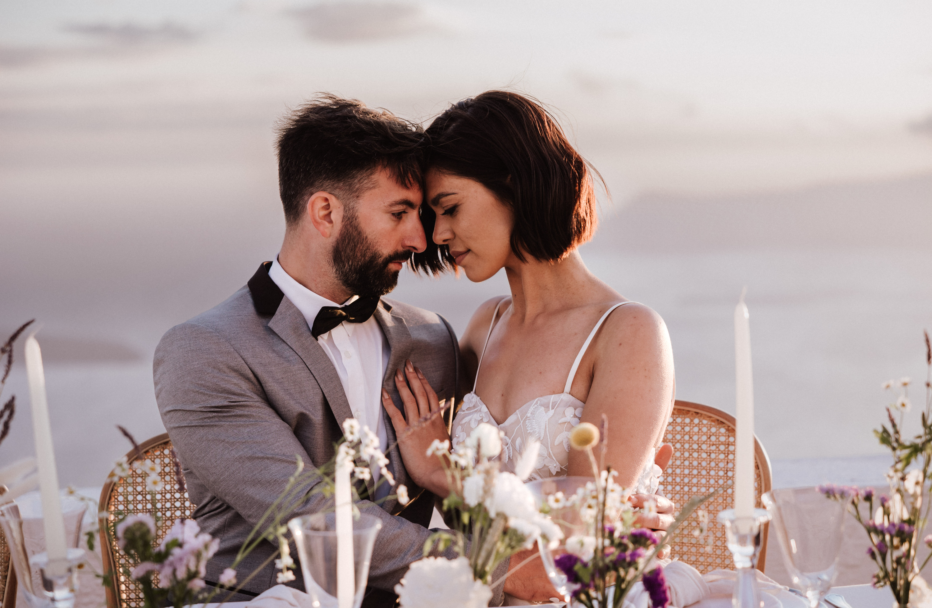 Das Brautpaar sitzt am Hochzeitstisch und blickt einander verliebt eng umschlungen an