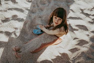 Etwa 8-jähriges Mädchen am Strand sitzend, die Beine mit Sand bedeckt