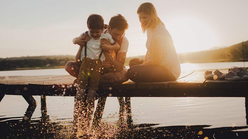 Familie im Sommer am See. Vater, Kind und schwangere Frau genießen den Sommer am Wasser.