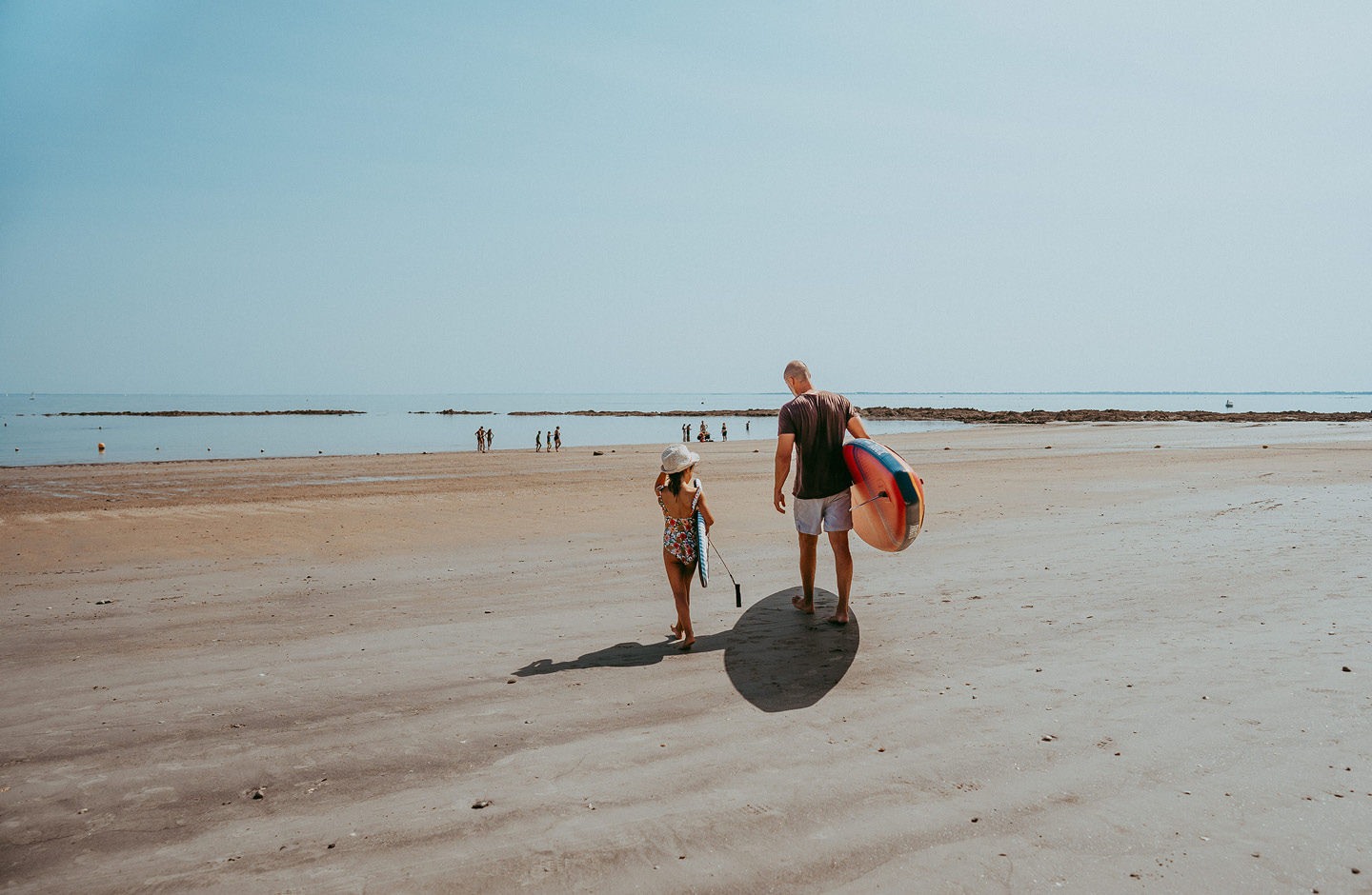 Vater mit seiner etwa 8-jährigen Tochter am Strand auf dem Weg ins Wasser