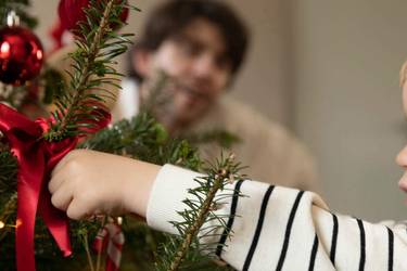 Kleiner Junge hängt Weihnachtsbaumschmuck auf.