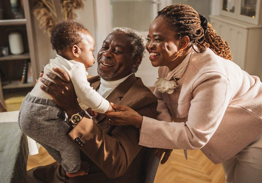 Großeltern halten stolz ihren Enkel am Tag der Namensgebungsfeier im Arm und lachen ihn an.