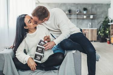 Happy pregnant woman with baby ultrasound photo embracing with her husband