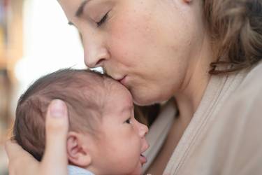 Übermüdete Mutter hält ihr Baby auf dem Arm und küsst es aufs Köpfchen