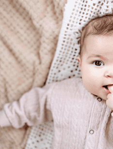 Kleines Mädchen in rosa Wolljacke mit gehäkelter Spitzendecke