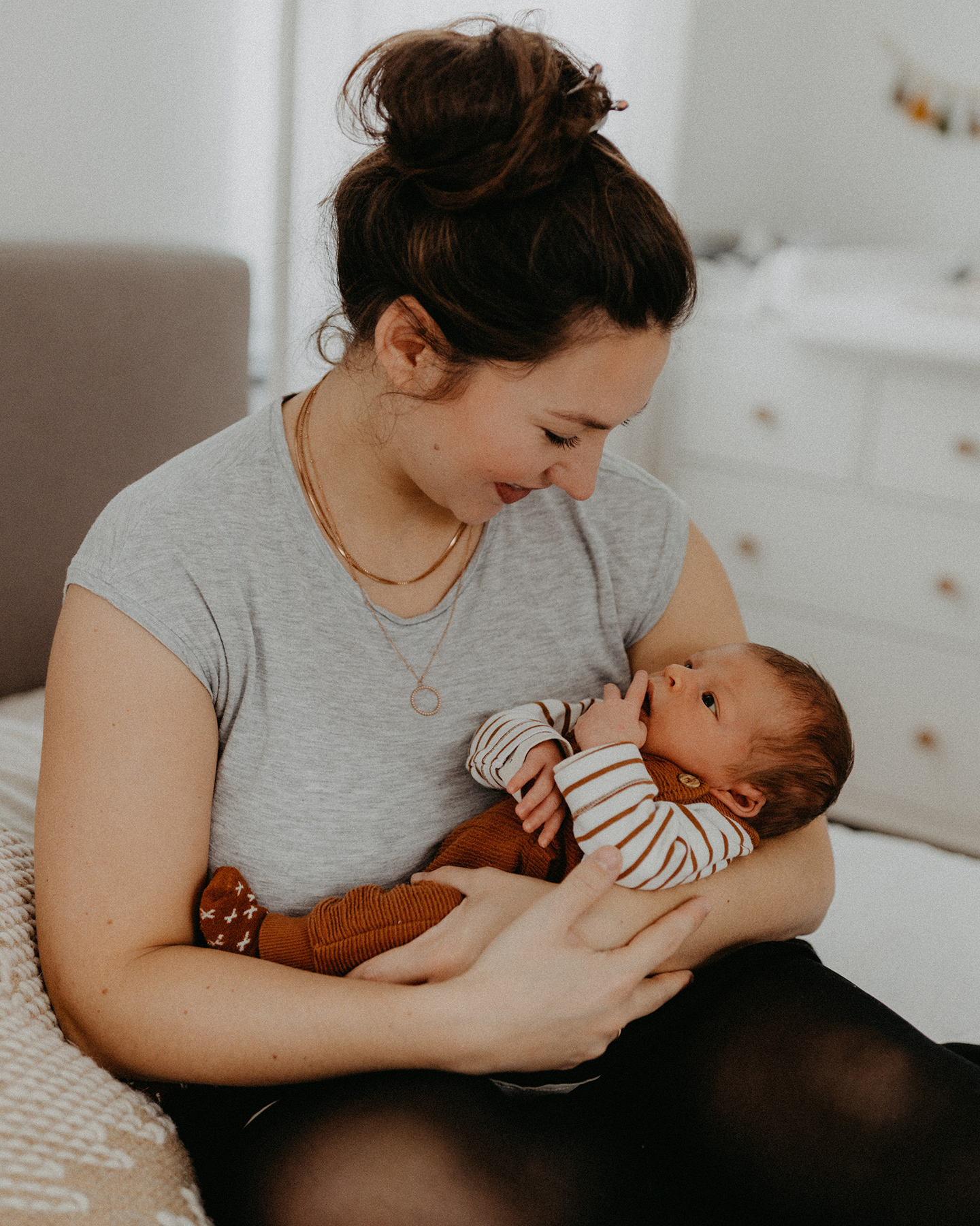 Mutter hält ihr Baby im Arm während sie auf dem Bett sitzt. 