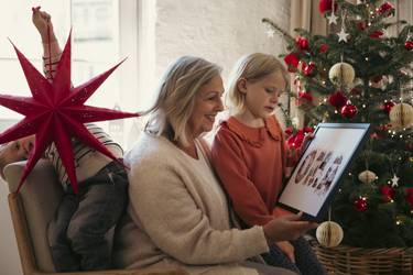 Oma sitzt mit zwei Kindern vor dem Weihnachtsbaum und schaut ein Bild an.