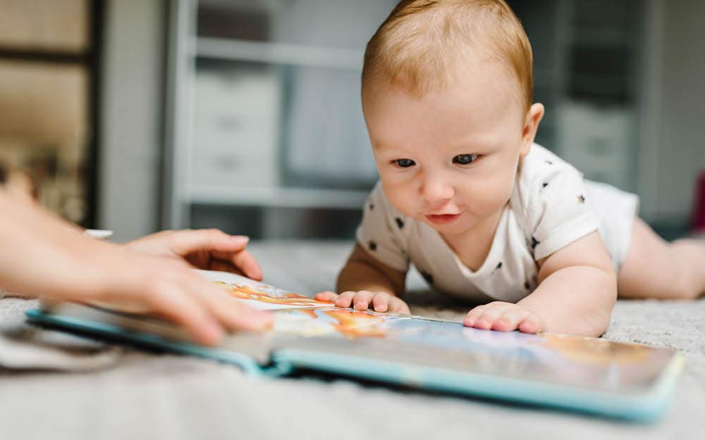 Baby schaut ein Bilderbuch auf dem Bauch liegend an