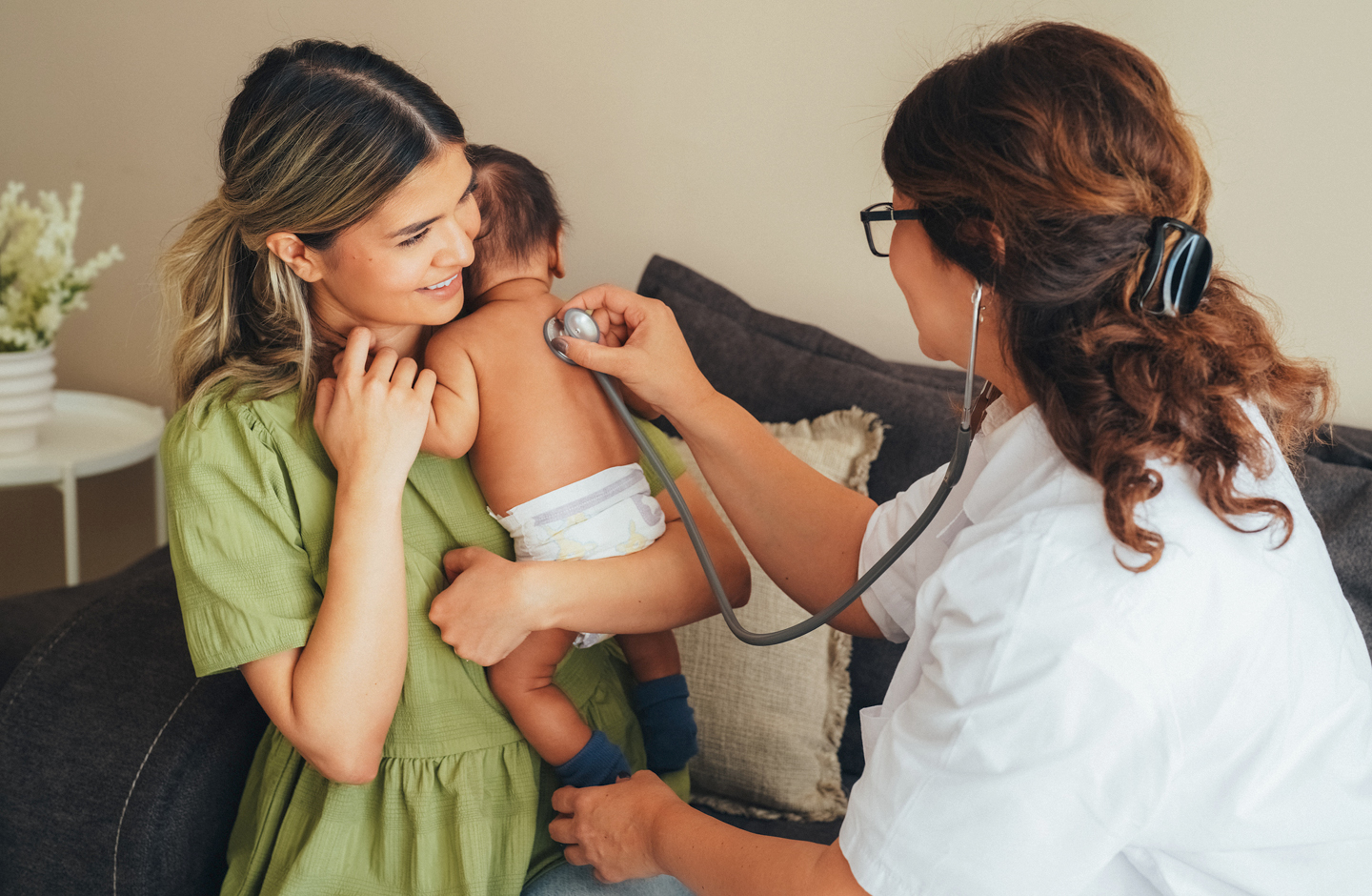 Eine Nachsorgehebamme untersucht Neugeborenes auf dem Arm der Mutter