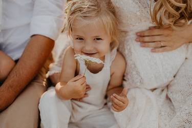 Kleines Mädchen im Sommer mit einer Blume in der Hand, sitzt zwischen seinem Vater und seiner schwangeren Mutter, die Eltern sind nicht ganz im Bild
