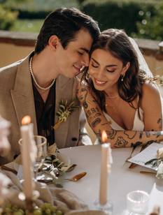 Das Hochzeitspaar sitzt zusammen am Tisch in der Hochzeitslocation in der Toskana und schaut verliebt. Der Tisch ist geschmückt mit zur Location und zum Motto passenden Elementen.