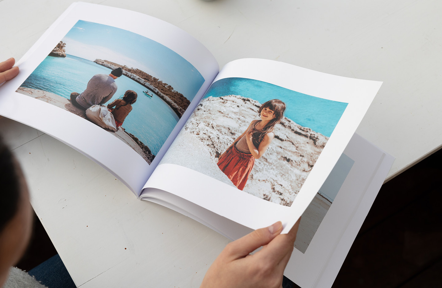 Frau (nicht im Bild) hält aufgeschlagenes Fotobuch mit Bildern aus dem Familienurlaub