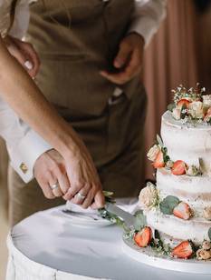 Brautpaar schneidet die drei stöckige Hochzeitstorte an, die mit Blumen und frischen Erdbeeren verziert ist