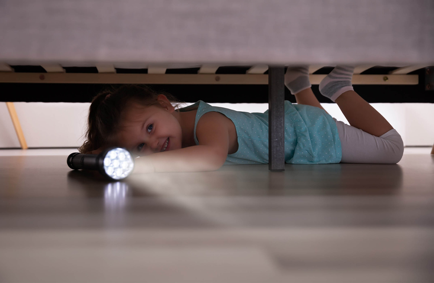 Kind leuchtet mit einer Taschenlampe unter das Bett