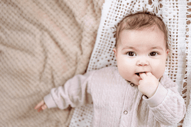 Kleines Mädchen in rosa Wolljacke mit gehäkelter Spitzendecke