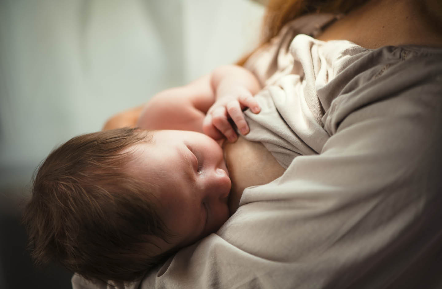 Baby trinkt mit geschlossenen Augen an der Brust der Mutter