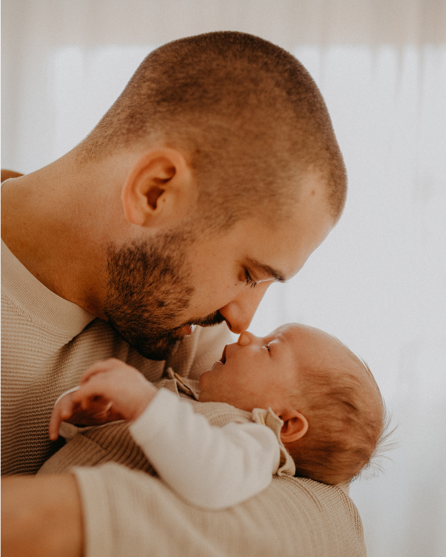 Glücklicher Vater hält zärtlich sein Neugeborenen im Arm, die Gesichter Nase an Nase