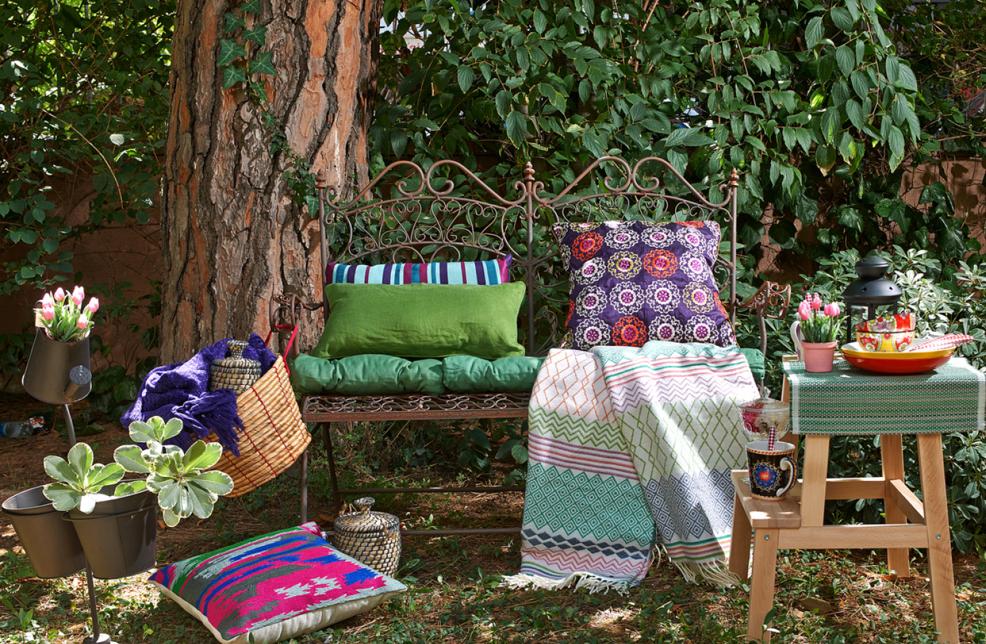 Gartenbank mit bunten Kissen und Decken.