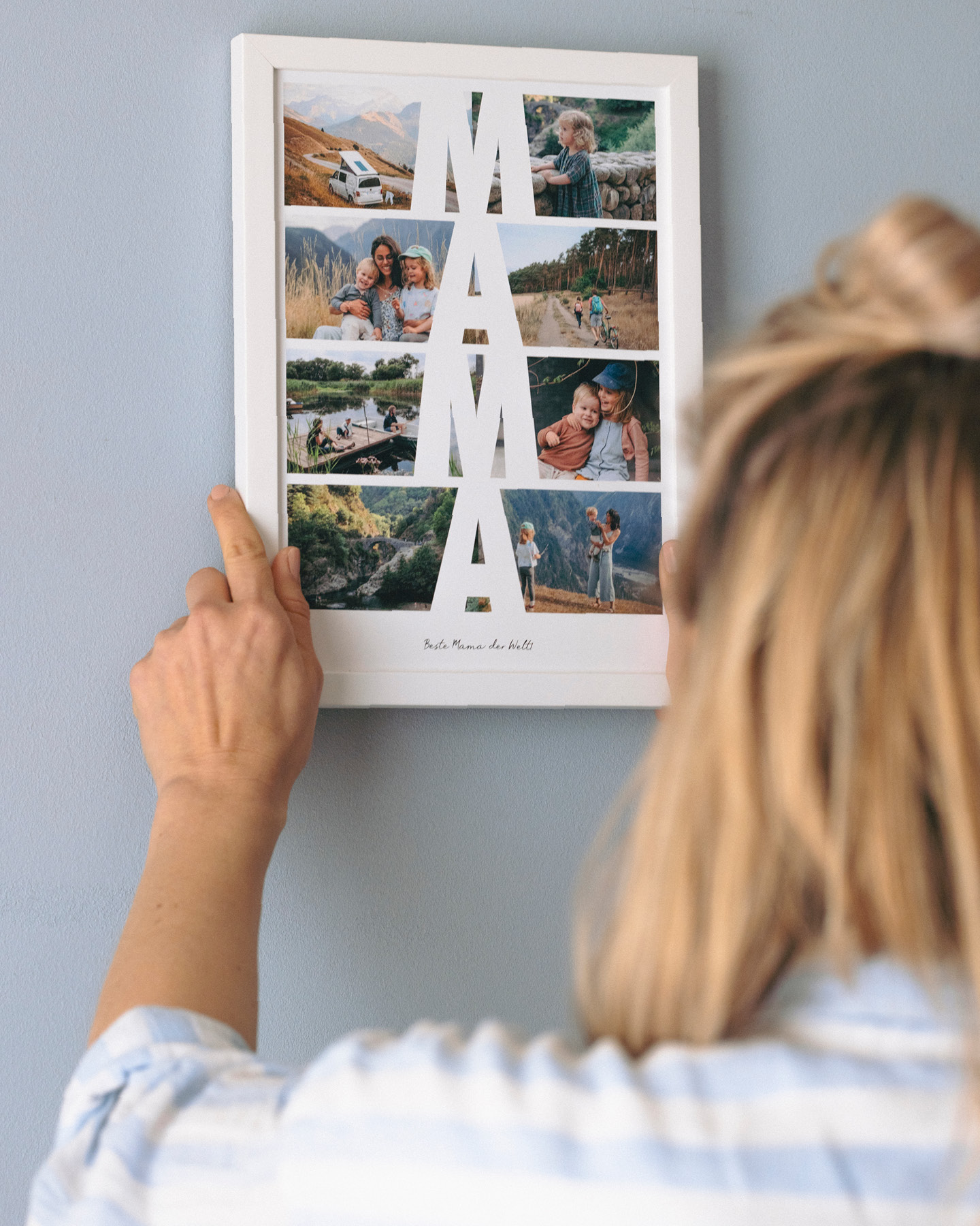 Junge Mutter berührt ihr Muttertagsgeschenk, ein gerahmtes Poster, das an der Wand hängt