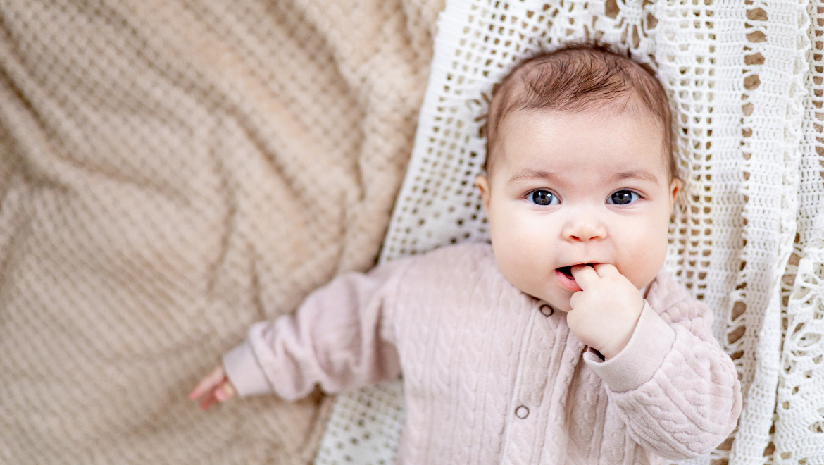 Kleines Mädchen in rosa Wolljacke mit gehäkelter Spitzendecke
