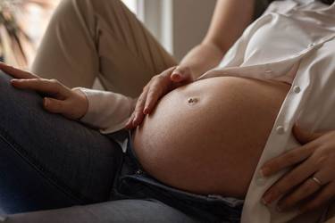 Hochschwangere Frau legt zärtlich ihre Hände auf ihren Babybauch