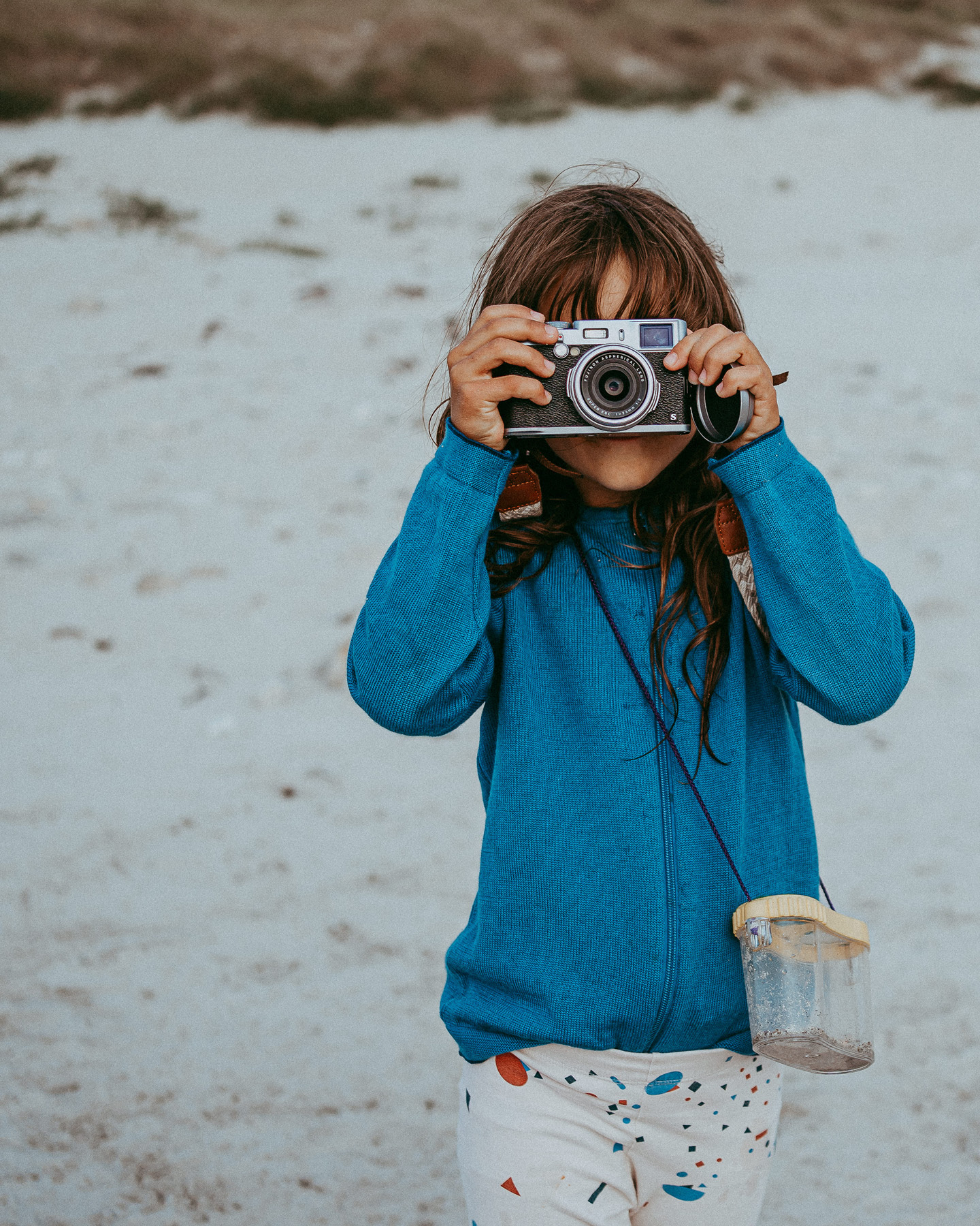 Mädchen am Strand mit Kamera vorm Gesicht