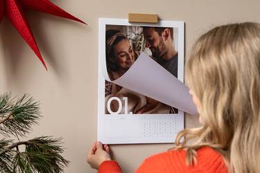Fotokalender hängt an der Wand. Frau blättert die erste Seite des Kalenders um.