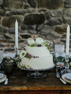 Hochzeitstafel mit blütenverzierter Torte vor Natursteinmauer