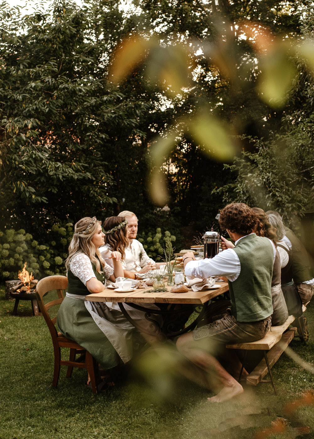 Eine gemütliche Runde aus Gästen und Hochzeitspaar sitzt im Garten und freut sich über den Kuchen. 