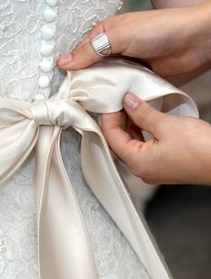 Nahaufnahme weibliche Hände beim Biden einer Satinschleife am Hochzeitskleid