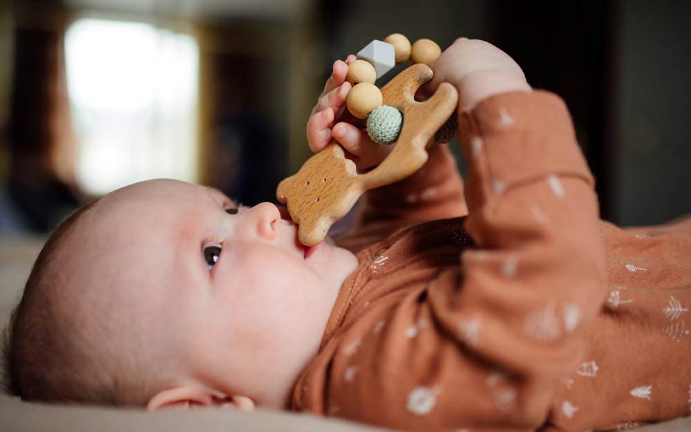 Baby hält Beißring aus Holz in den Händen