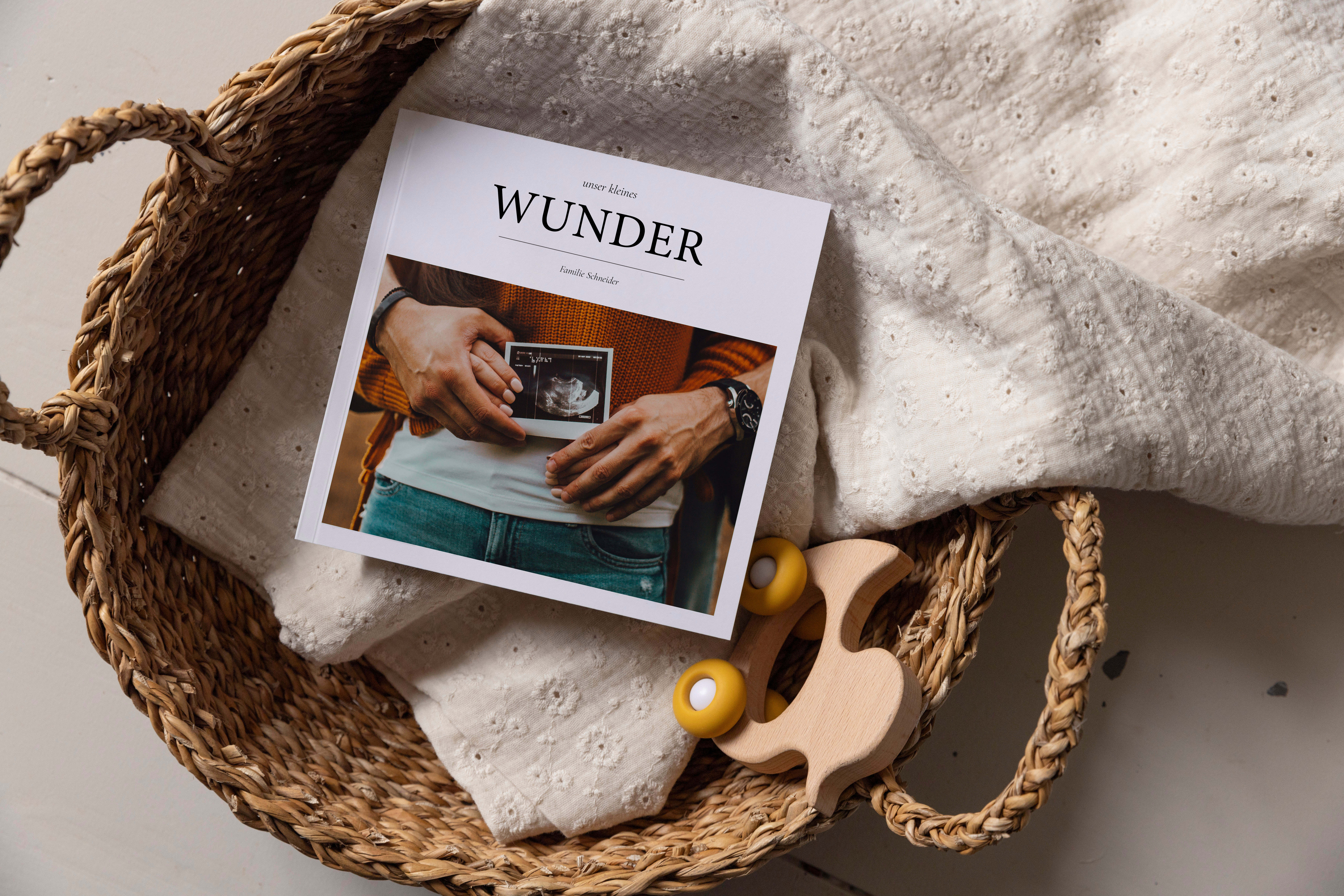Fotobuch von der Schwangerschaft in einem Korb mit Babydecke und Spielzeug