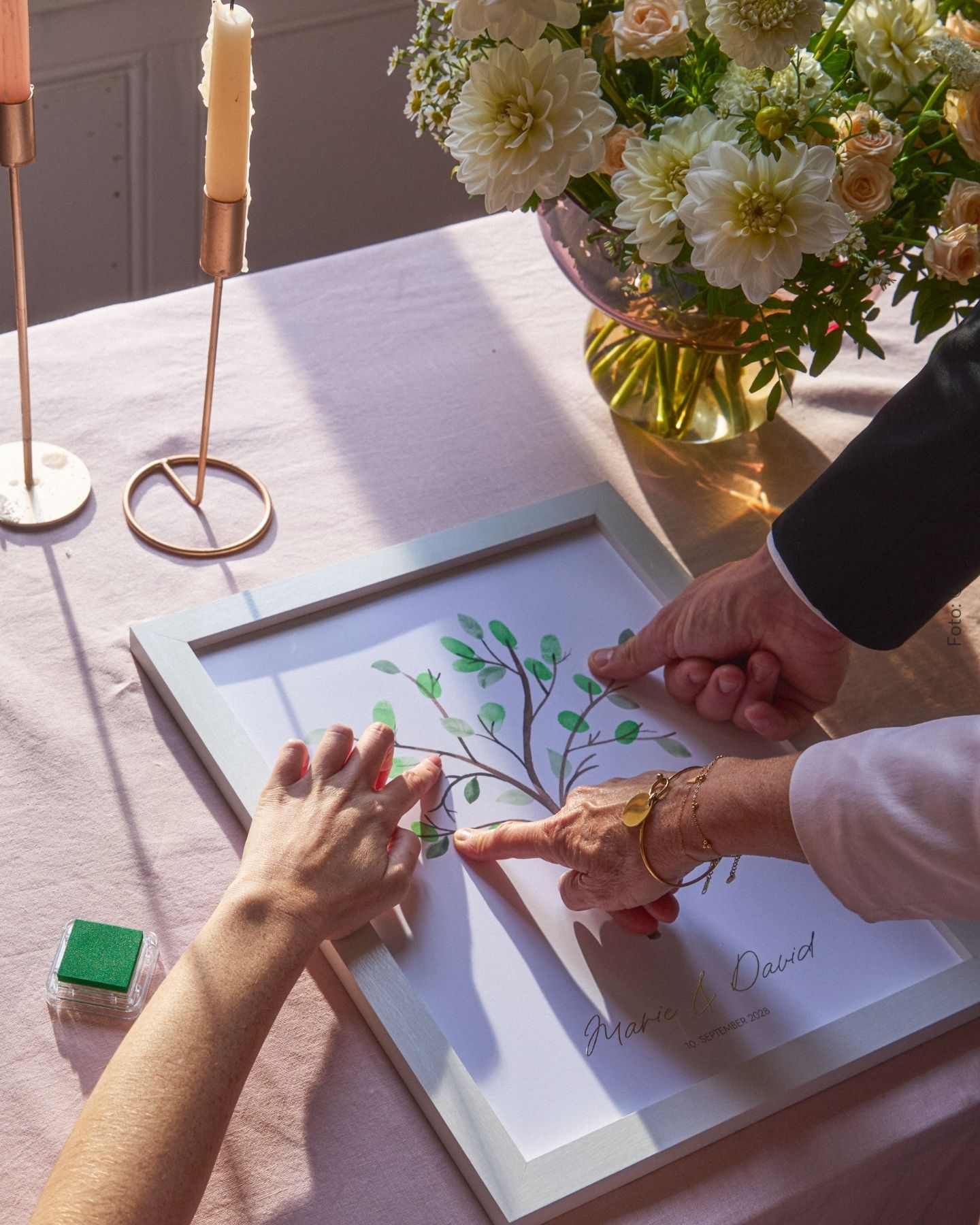 Hochzeitsgäste stempeln mit den Fingern Blätter auf ein Fingerabdruckbild mit Baummotiv