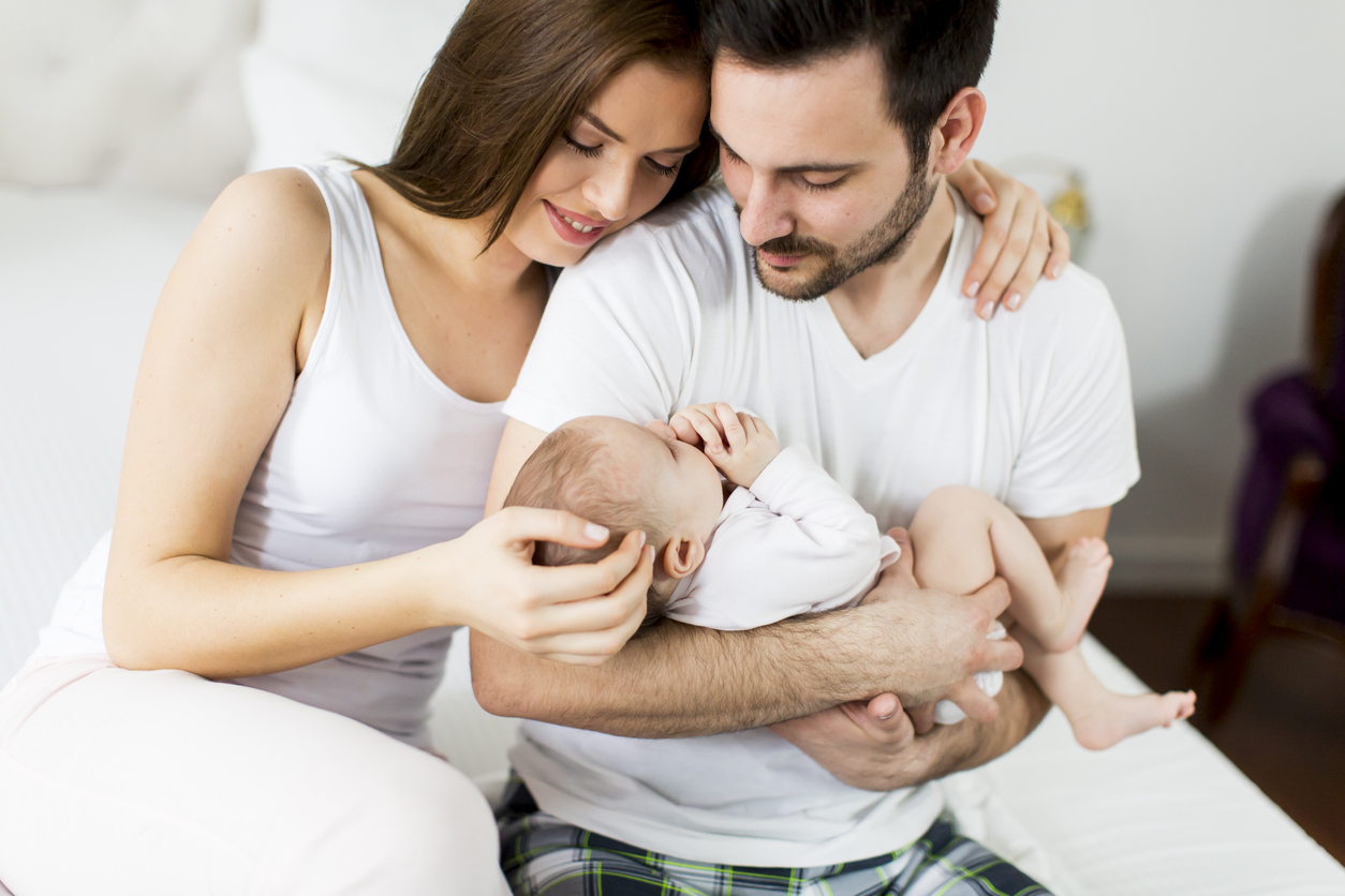 Junge Mutter umarmt jungen Papa mit Baby auf dem Arm