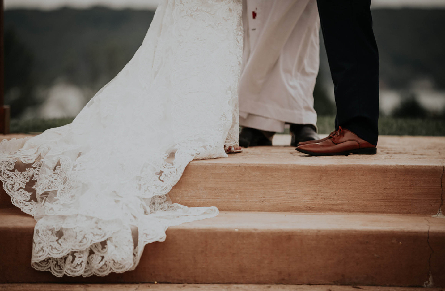 Ein Brautpaar steht sich auf einer Treppenstufe gegenüber. Abgebildet sind nur die Beine des Bräutigams und die lange weiße Schleppe des Brautkleides der Braut. 
